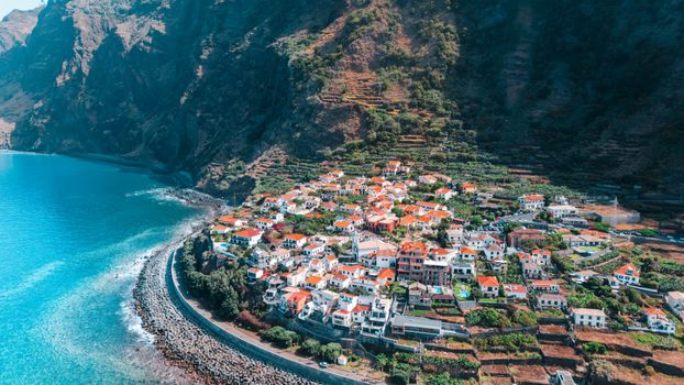 Stunning aerial view of a coastal town in Madeira, Portugal, with lush cliffs and turquoise sea.