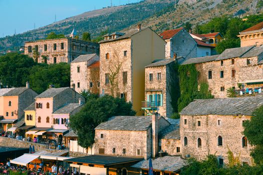 Explore the rustic charm of Mostar's historic stone buildings under a summer sky.