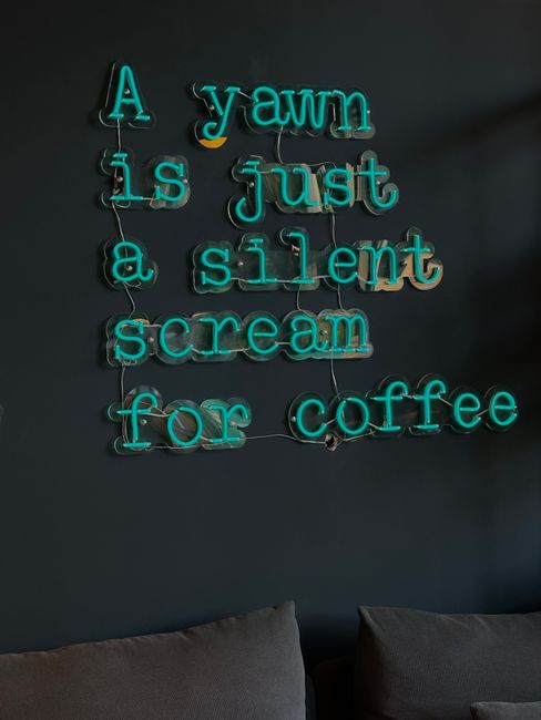 Green neon sign reading 'A yawn is just a silent scream for coffee' on dark wall.