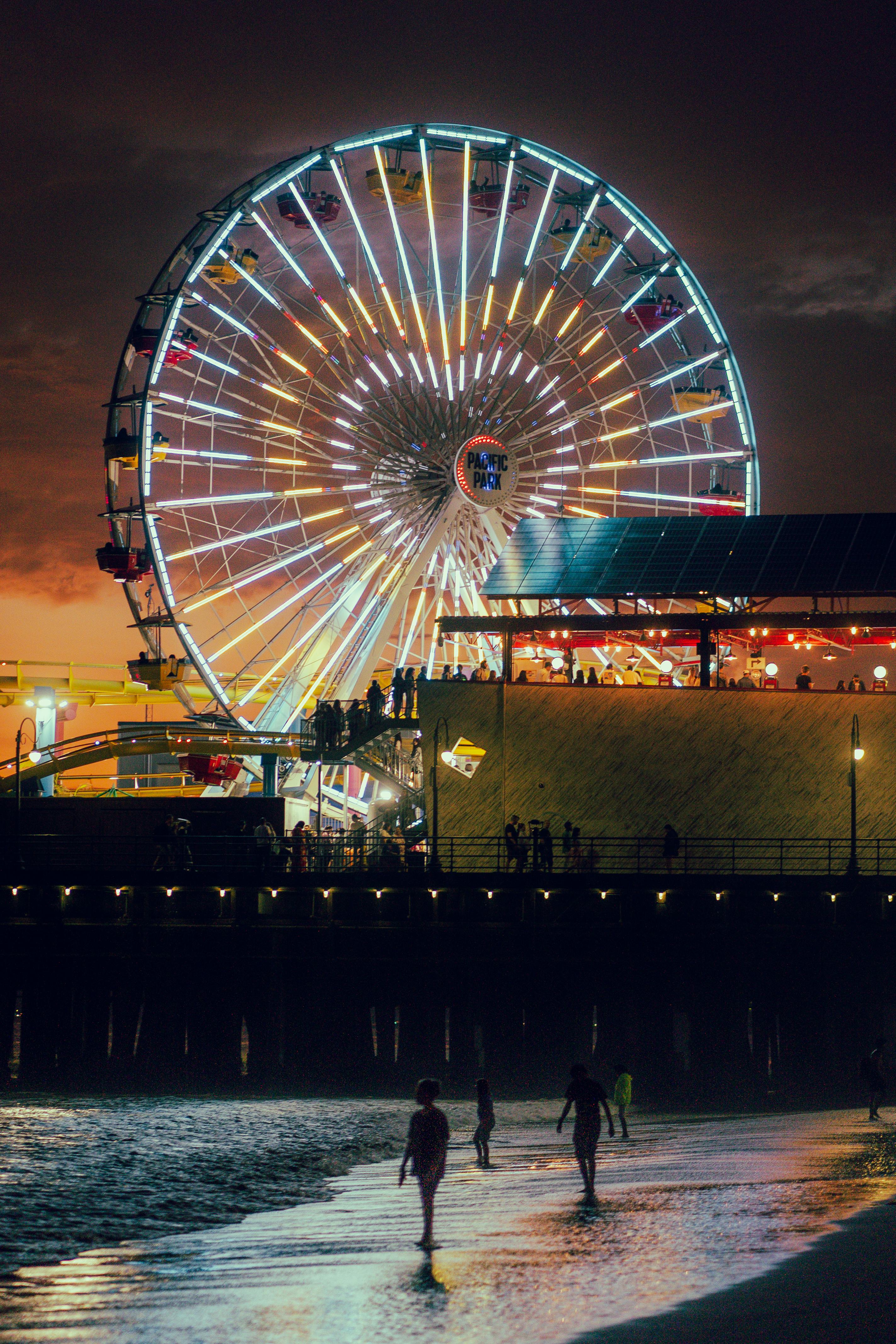A stunning view of the illuminated Ferris wheel at Santa Monica Pier during dusk, reflecting on the water.