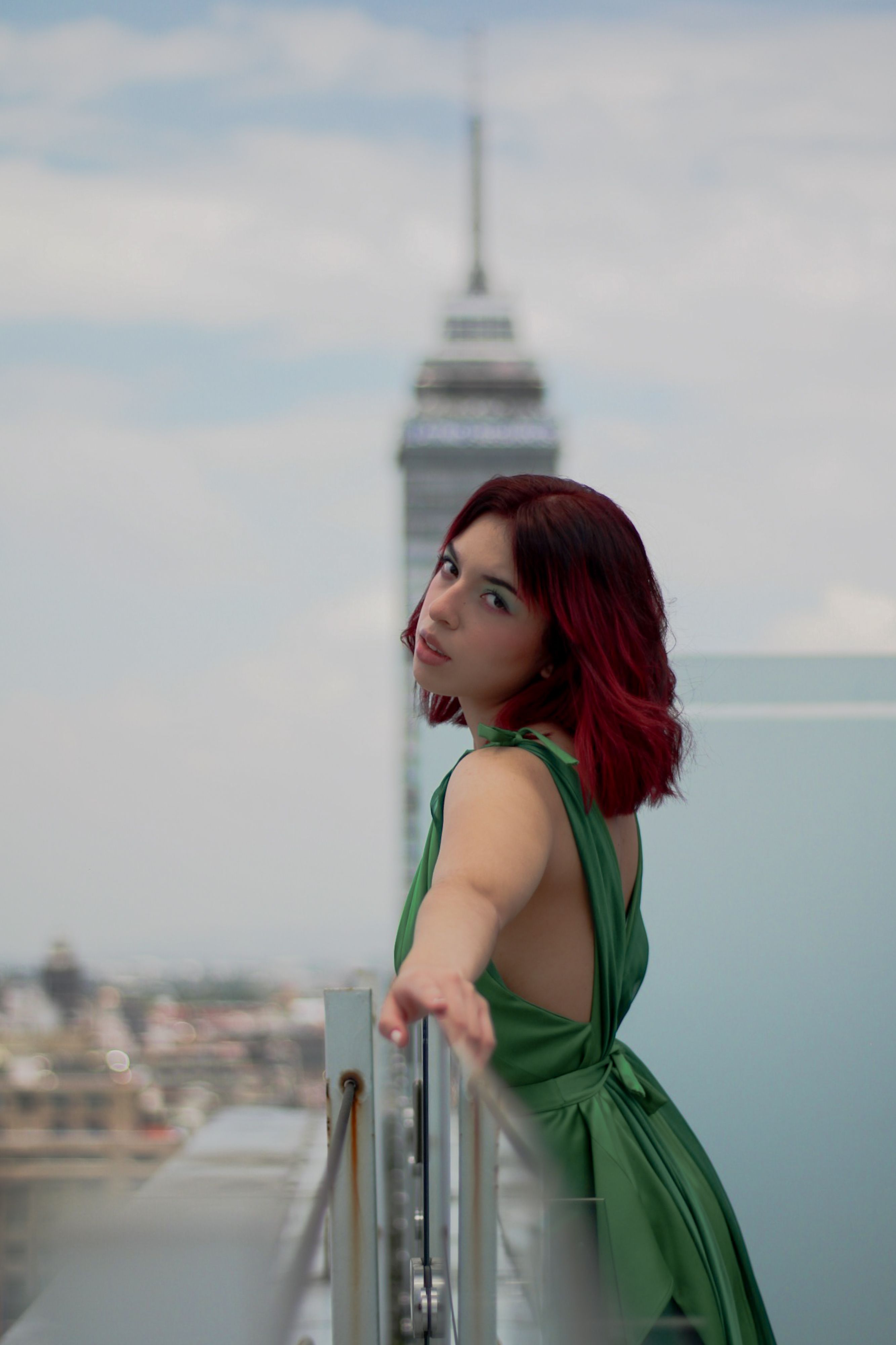 Woman in green dress posing on rooftop with city skyline in background