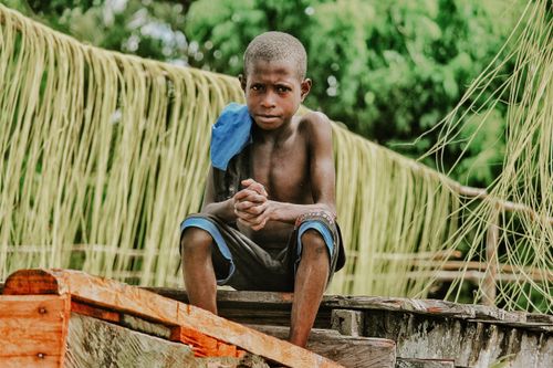 Free A young boy sits on wooden logs surrounded by natural greenery in Agats, Papua, Indonesia. Stock Photo