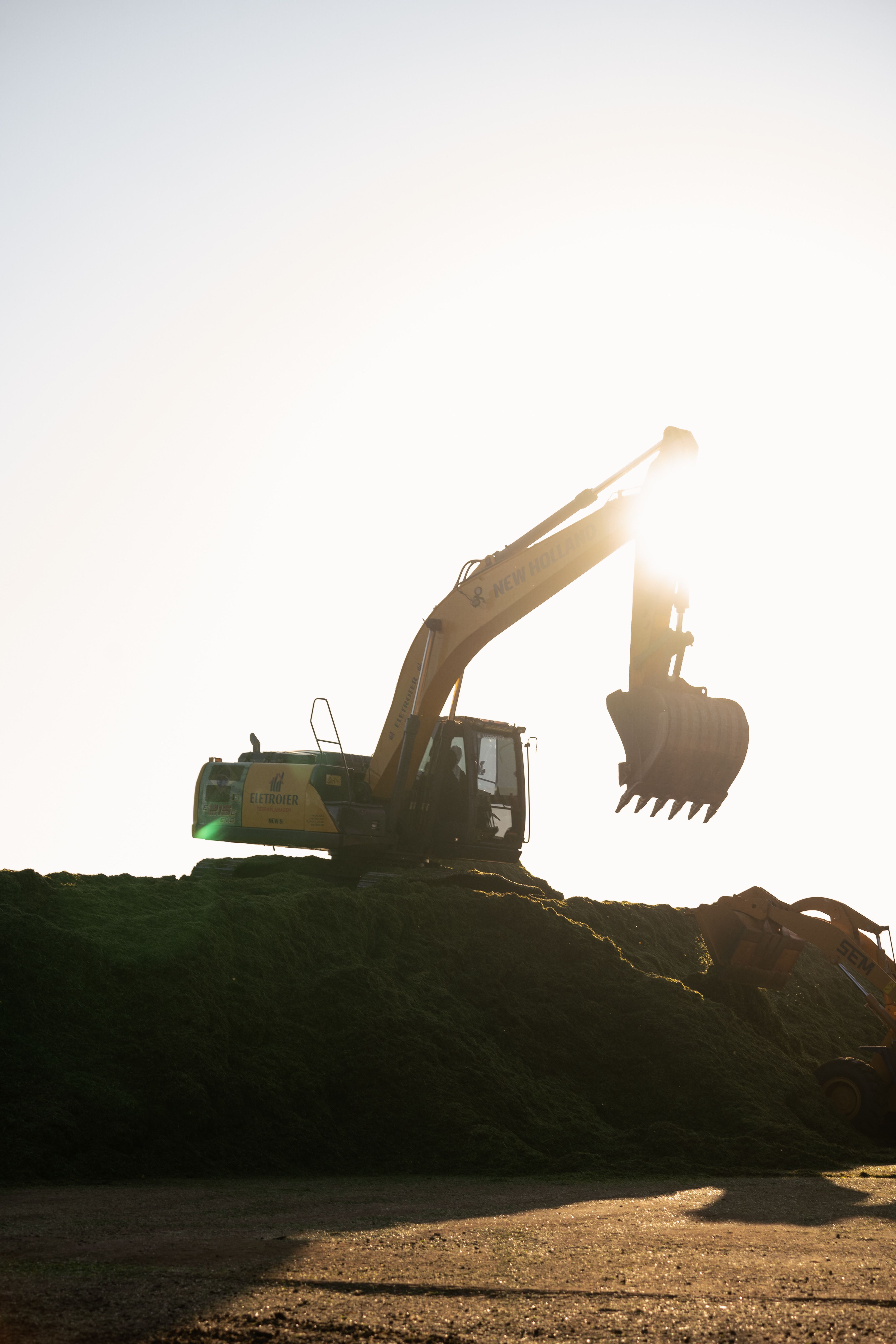 A silhouetted excavator on a dirt pile at sunset.