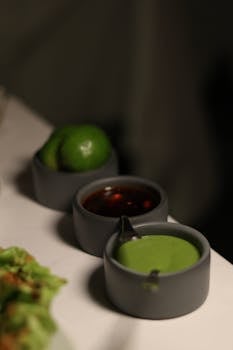 A trio of sauces with lime on a white table create an inviting culinary scene.