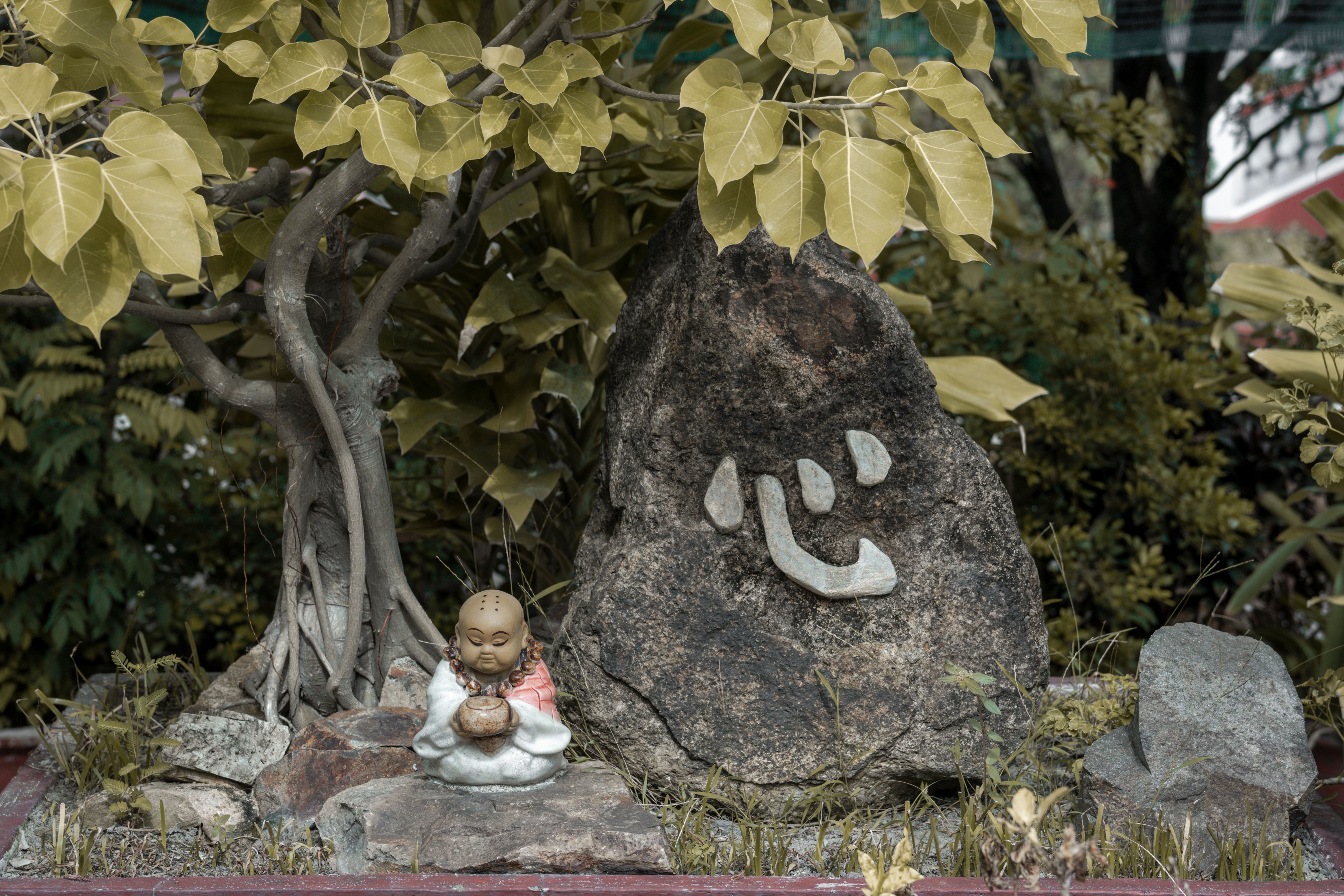 A small statue of a buddha sitting on a rock · Free Stock Photo