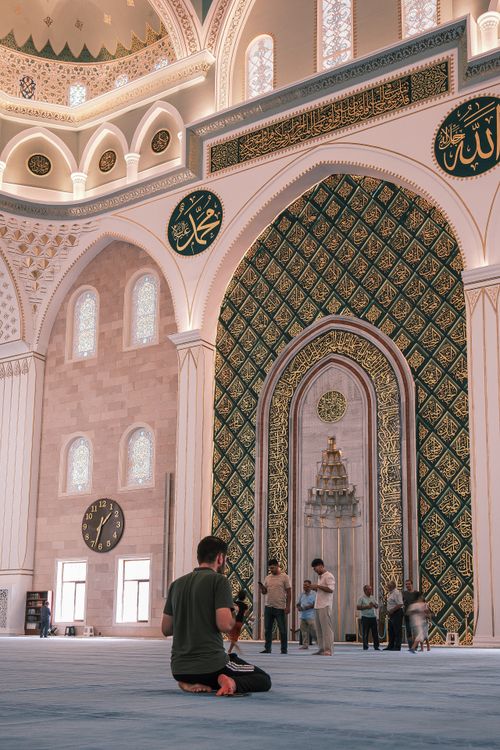 Free Beautiful mosque interior with intricate decorations and worshippers in peaceful prayer setting. Stock Photo