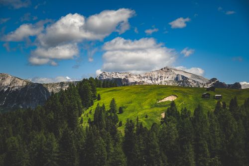 Free Beautiful alpine landscape featuring rolling green meadows, dense forests, and rugged mountains under a bright blue sky. Stock Photo
