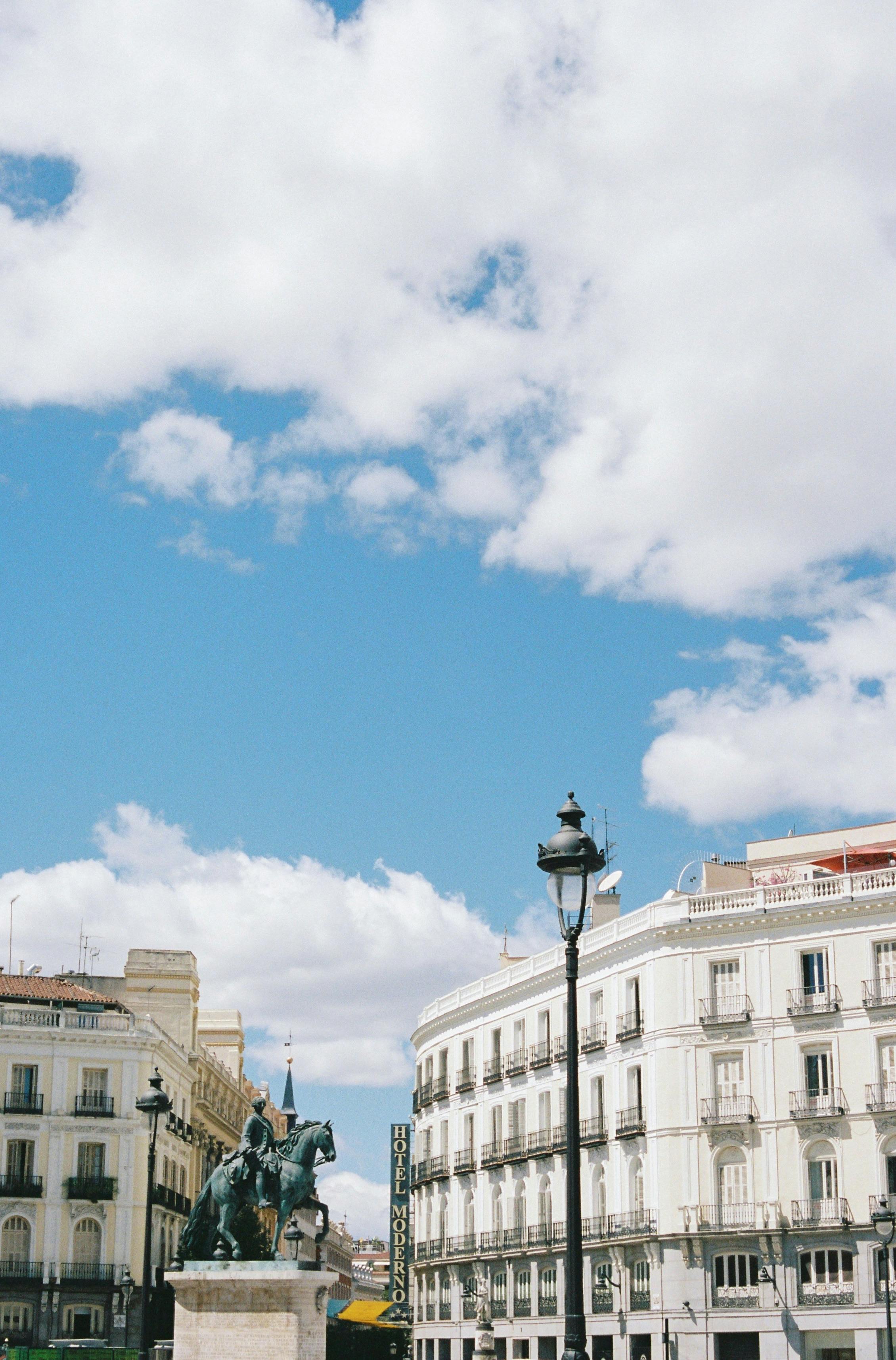 A scenic view of a historic plaza in Madrid, Spain, featuring classic architecture under a vibrant blue sky.