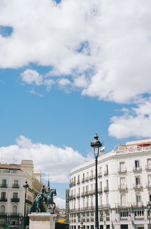 Free A scenic view of a historic plaza in Madrid, Spain, featuring classic architecture under a vibrant blue sky. Stock Photo