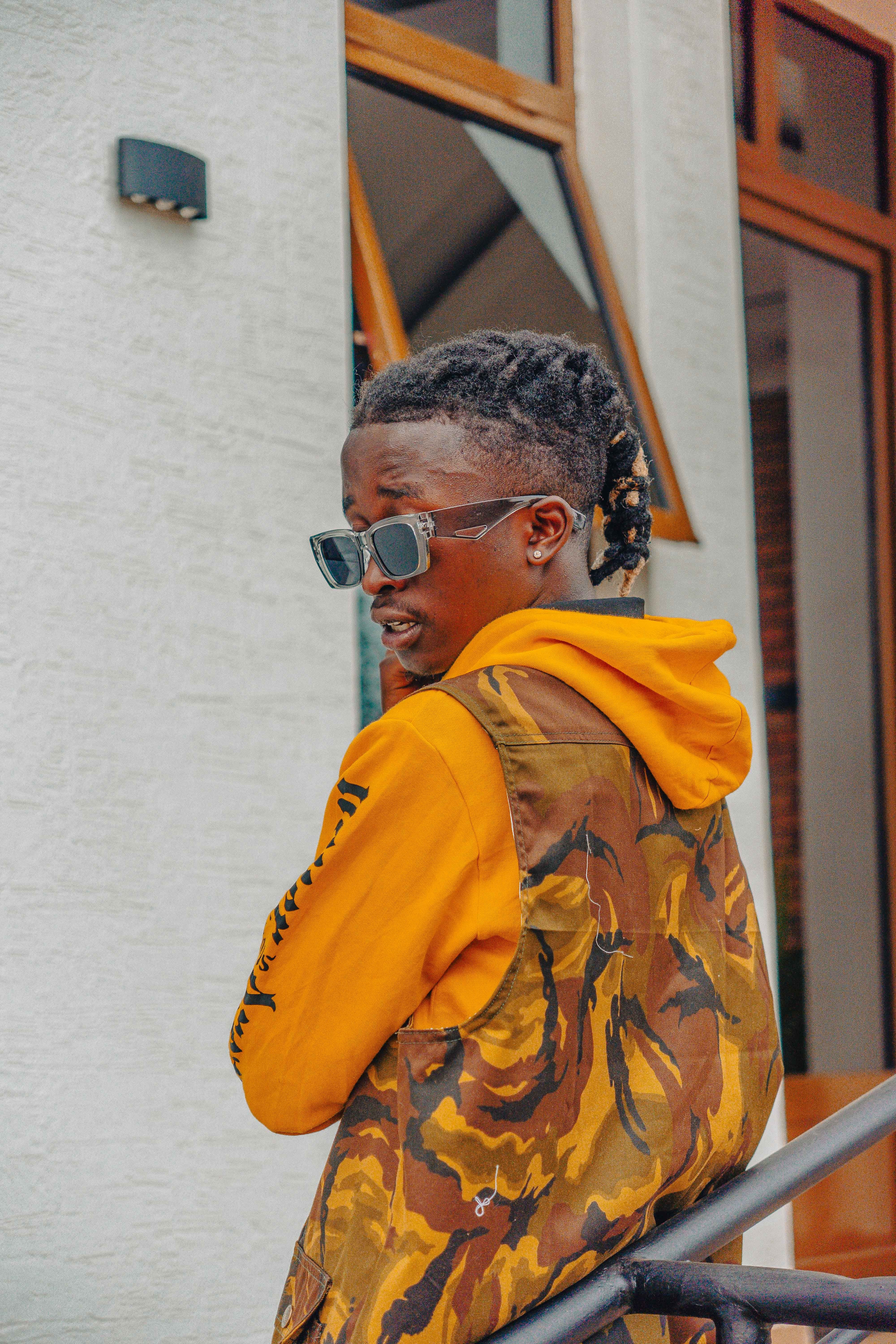 A trendy young man posing confidently outdoors in a colorful outfit with sunglasses.