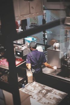 Young worker in an industrial kitchen preparing food, wearing a uniform.