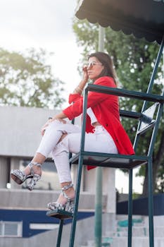 一位穿着红色西装外套的时尚女性坐在户外，戴着墨镜，散发着现代气息