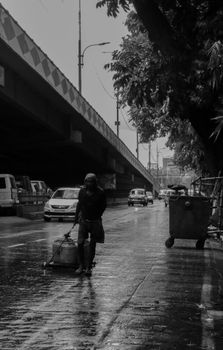 Monochrome image capturing a person pulling a cart on a rainy Kolkata street.