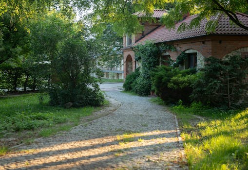 A picturesque view of a brick house surrounded by lush greenery and a stone path.