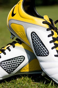 High-quality image of yellow and white soccer shoes with black laces on grass.