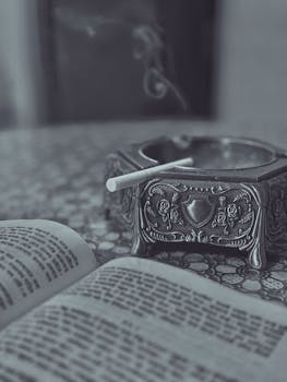 A vintage ashtray with a cigarette and an open book on a textured surface, evoking a retro feel.