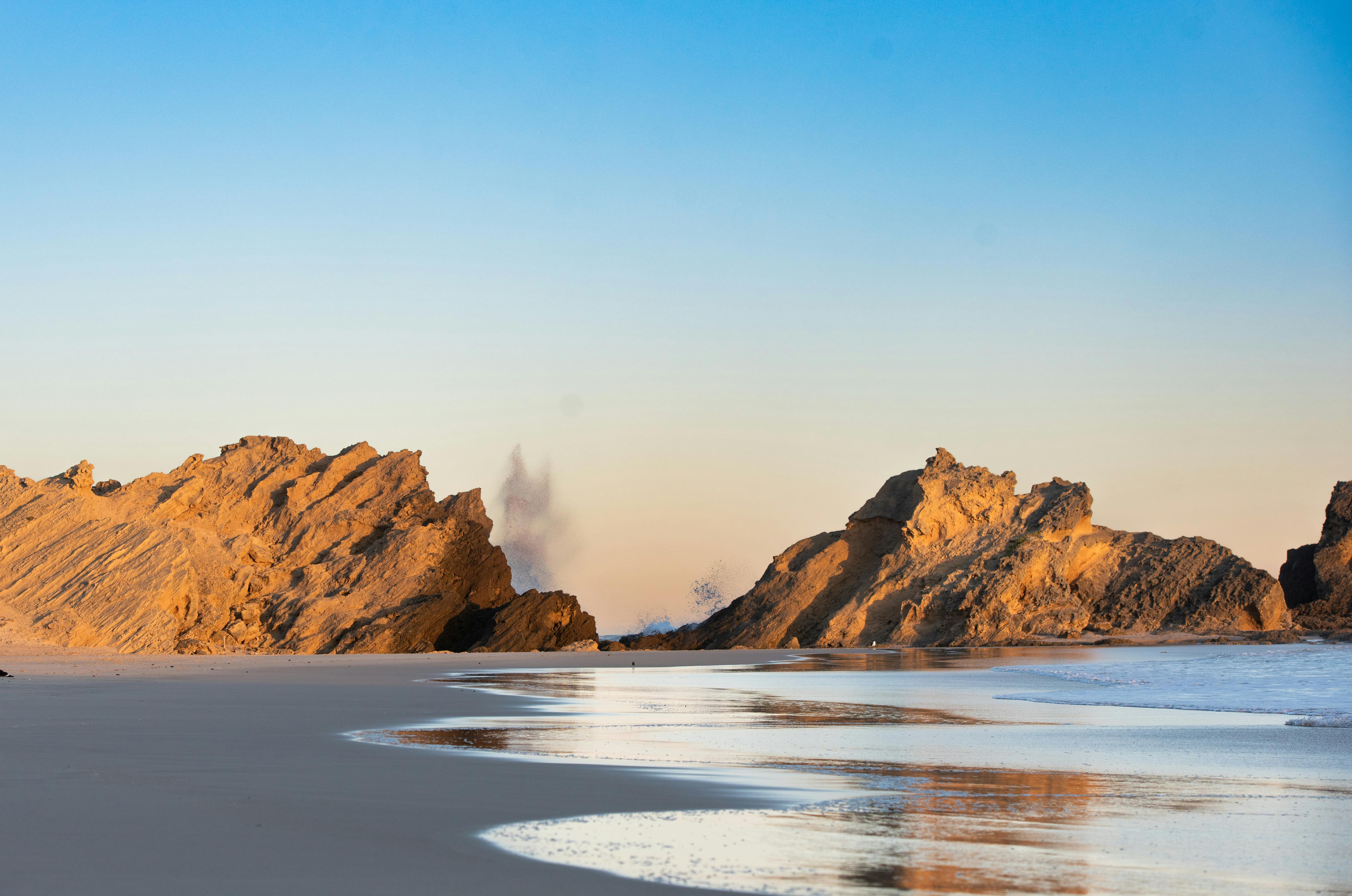 A serene view of cliffs and ocean with reflections on a sandy beach during dawn.