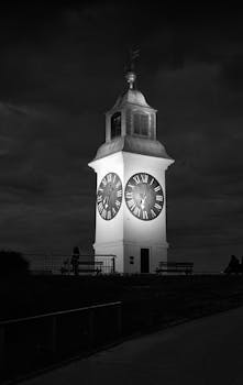 A dramatic night shot of the illuminated Petrovaradin Clock Tower under a moody sky, capturing its historical charm.