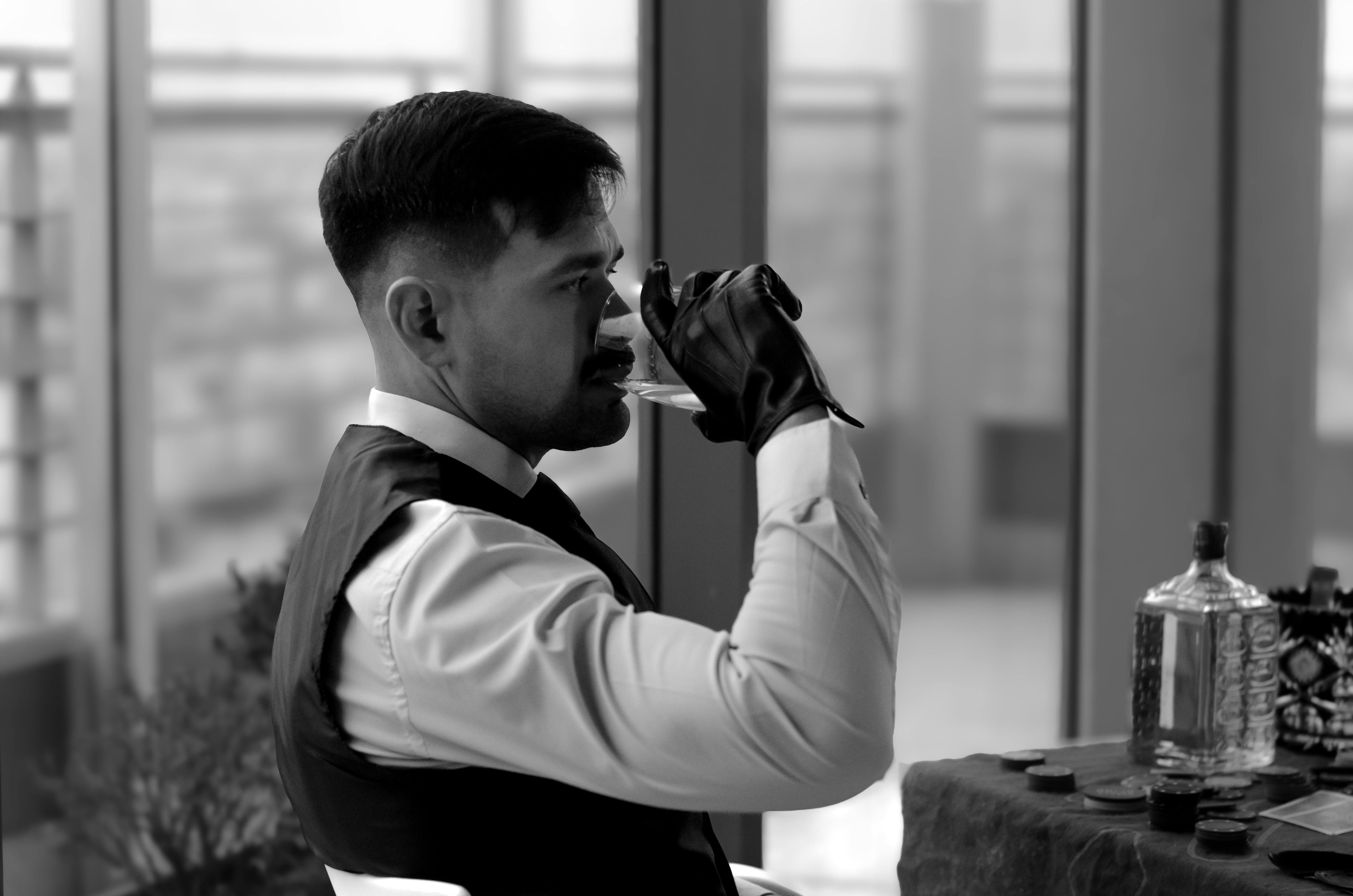 a man in a black tie and gloves drinking a drink