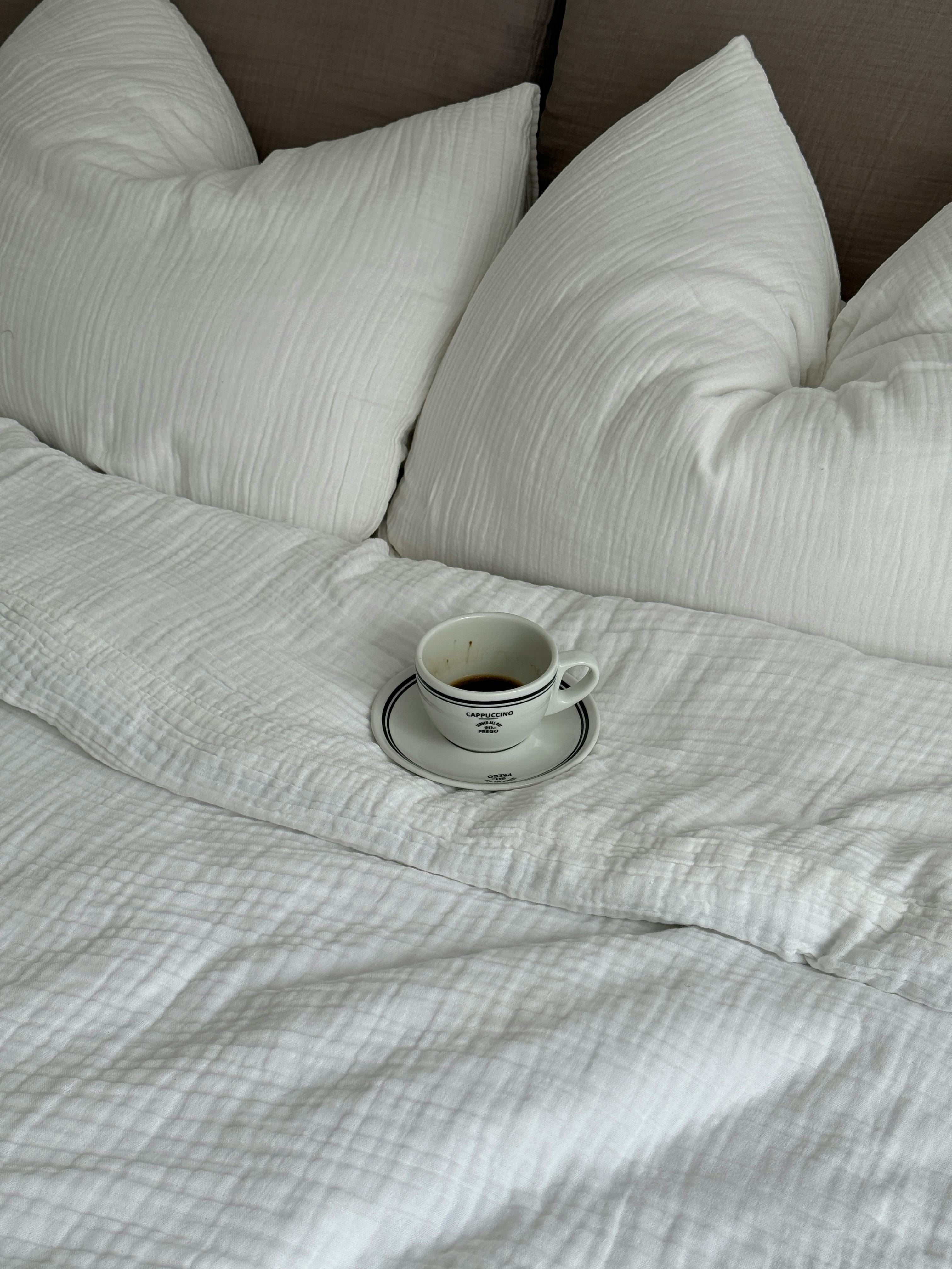 Elegant bedroom setting featuring white linens and a warm cup of coffee, evoking relaxation.