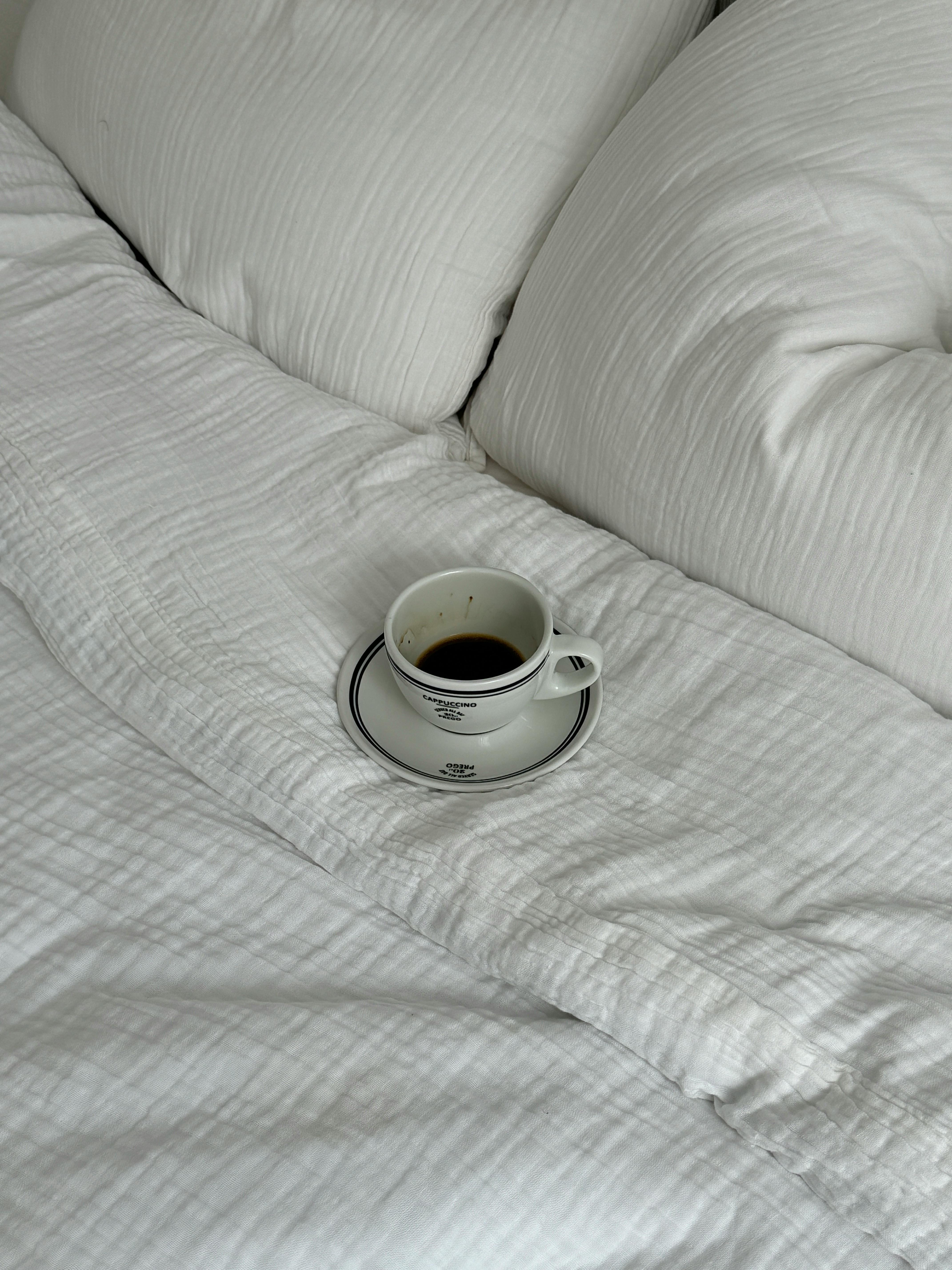 Cup of black coffee resting on comfortable white bedding, evoking morning relaxation.