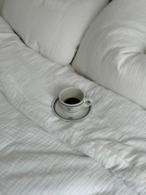 Free Cup of black coffee resting on comfortable white bedding, evoking morning relaxation. Stock Photo