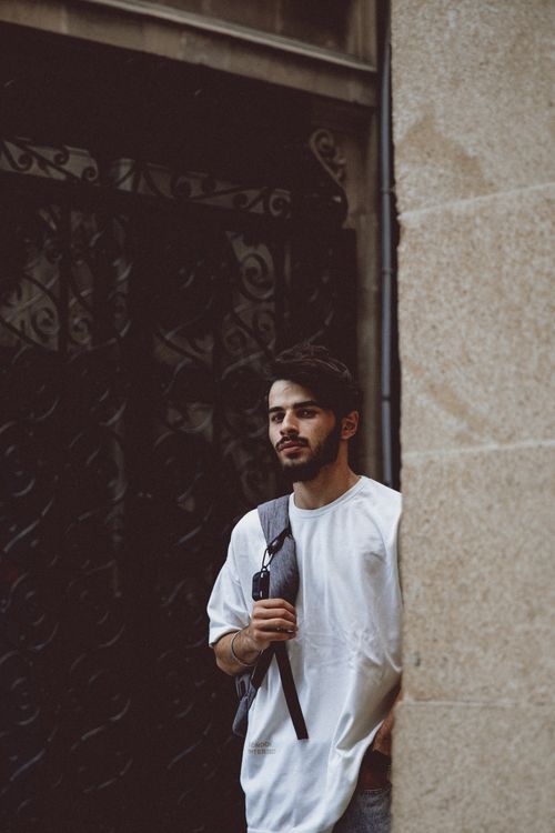 Free A young man with a backpack stands against a textured wall on a street in Baku, Azerbaijan. Stock Photo