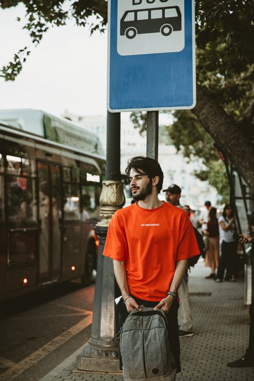 Free Young man in red shirt waiting at a bus stop in urban Baku, Azerbaijan, during the day. Stock Photo