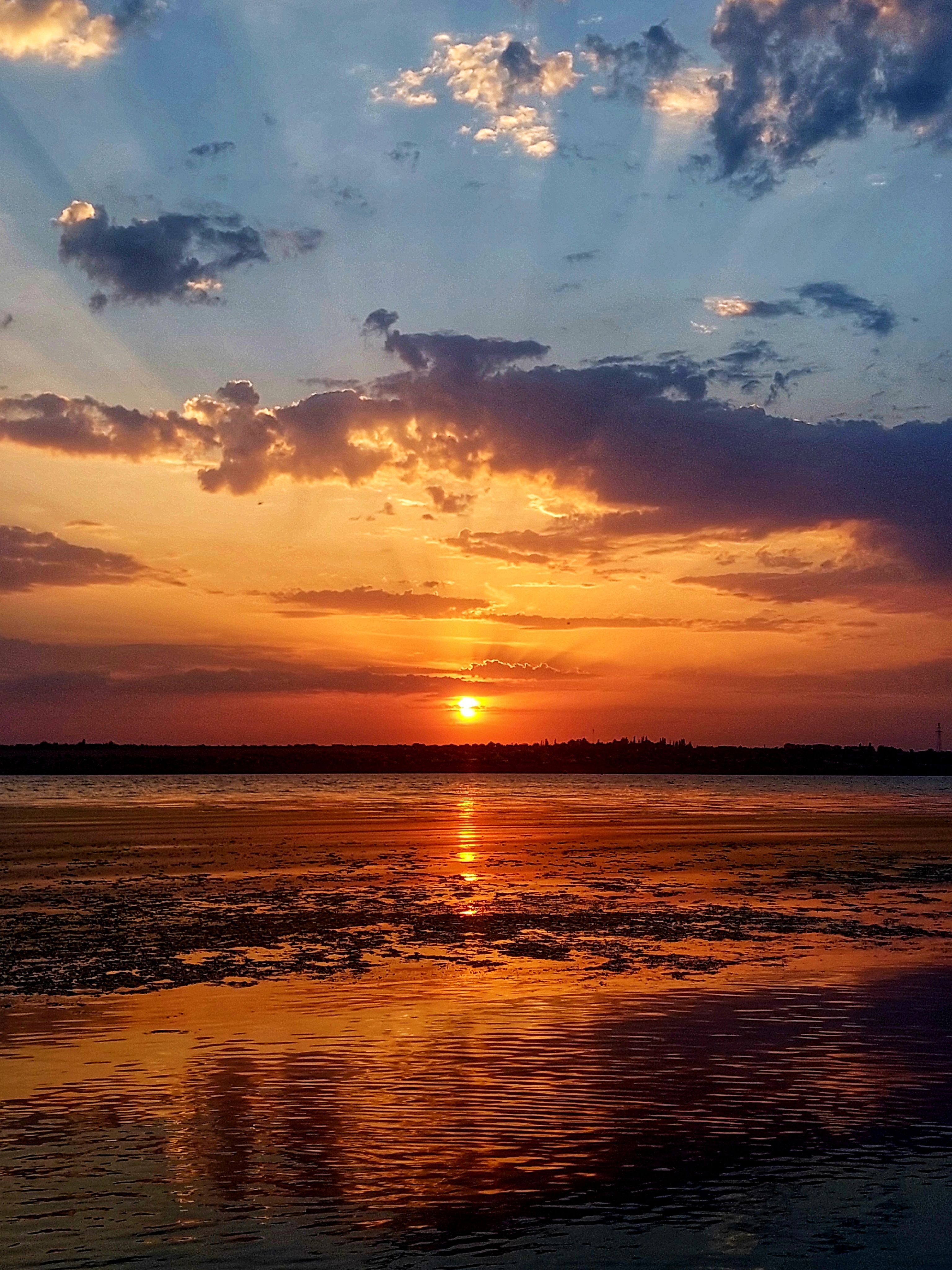 Sunset over the water with clouds and sun · Free Stock Photo