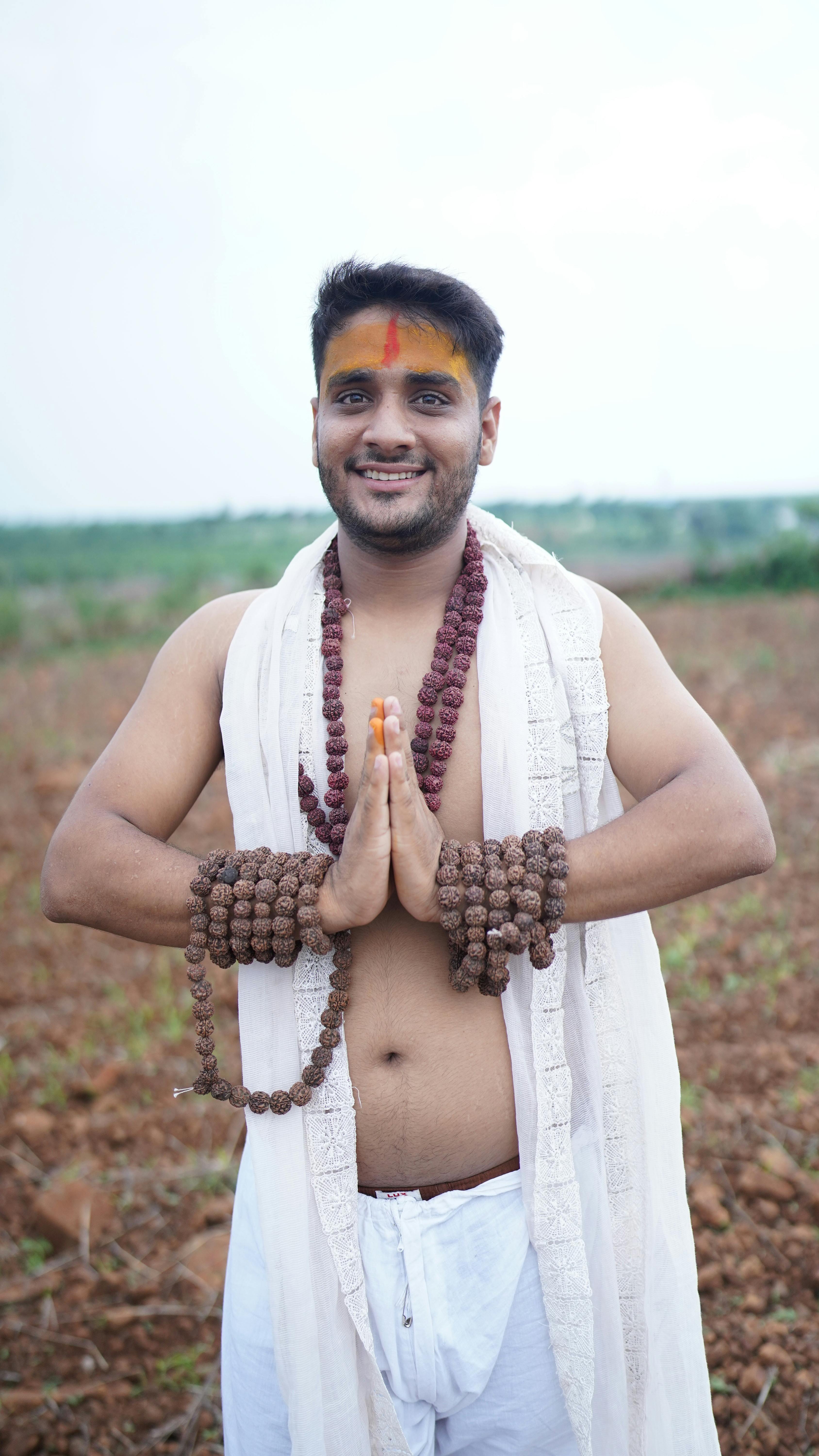 Smiling young man in traditional attire with prayer beads in open field showcasing cultural heritage.
