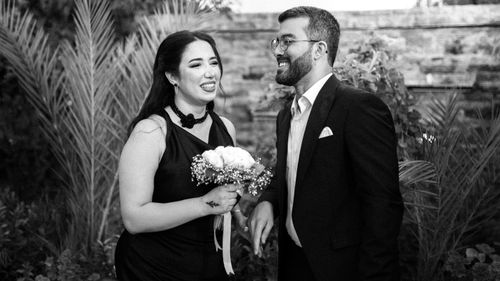 Free A joyous wedding couple shares a laugh in an elegant outdoor garden setting. Stock Photo