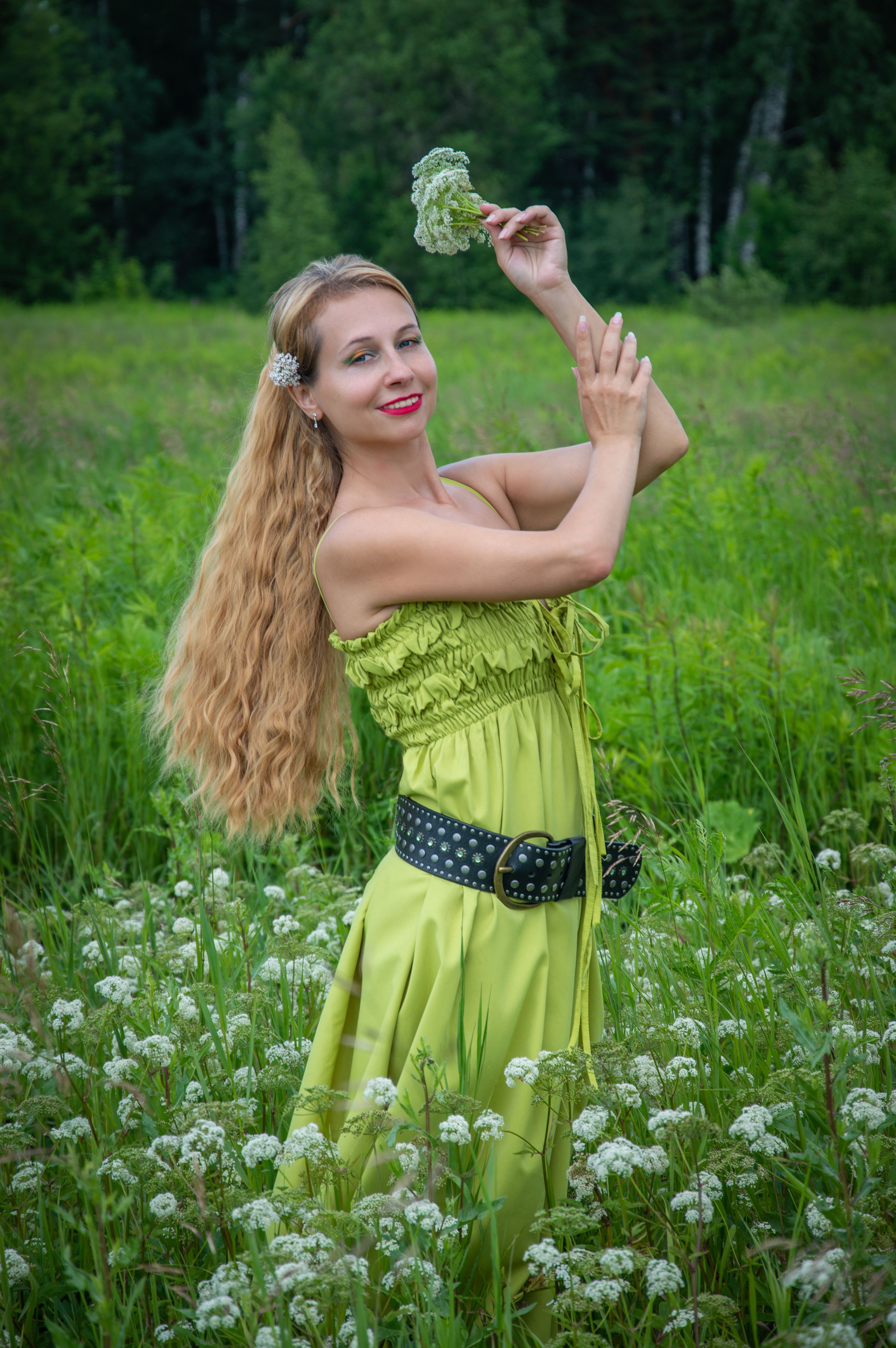 Woman enjoying a summer day in a lush green field with flowering plants, exuding joy and relaxation.