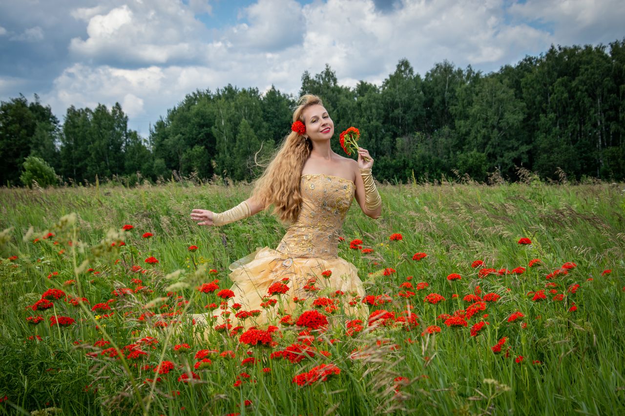 a woman in a field of red flowers enjoys the summer day expressing joy