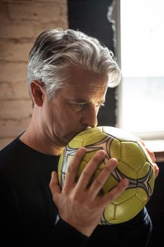 Portrait of an adult man indoors holding a soccer ball with a contemplative expression.
