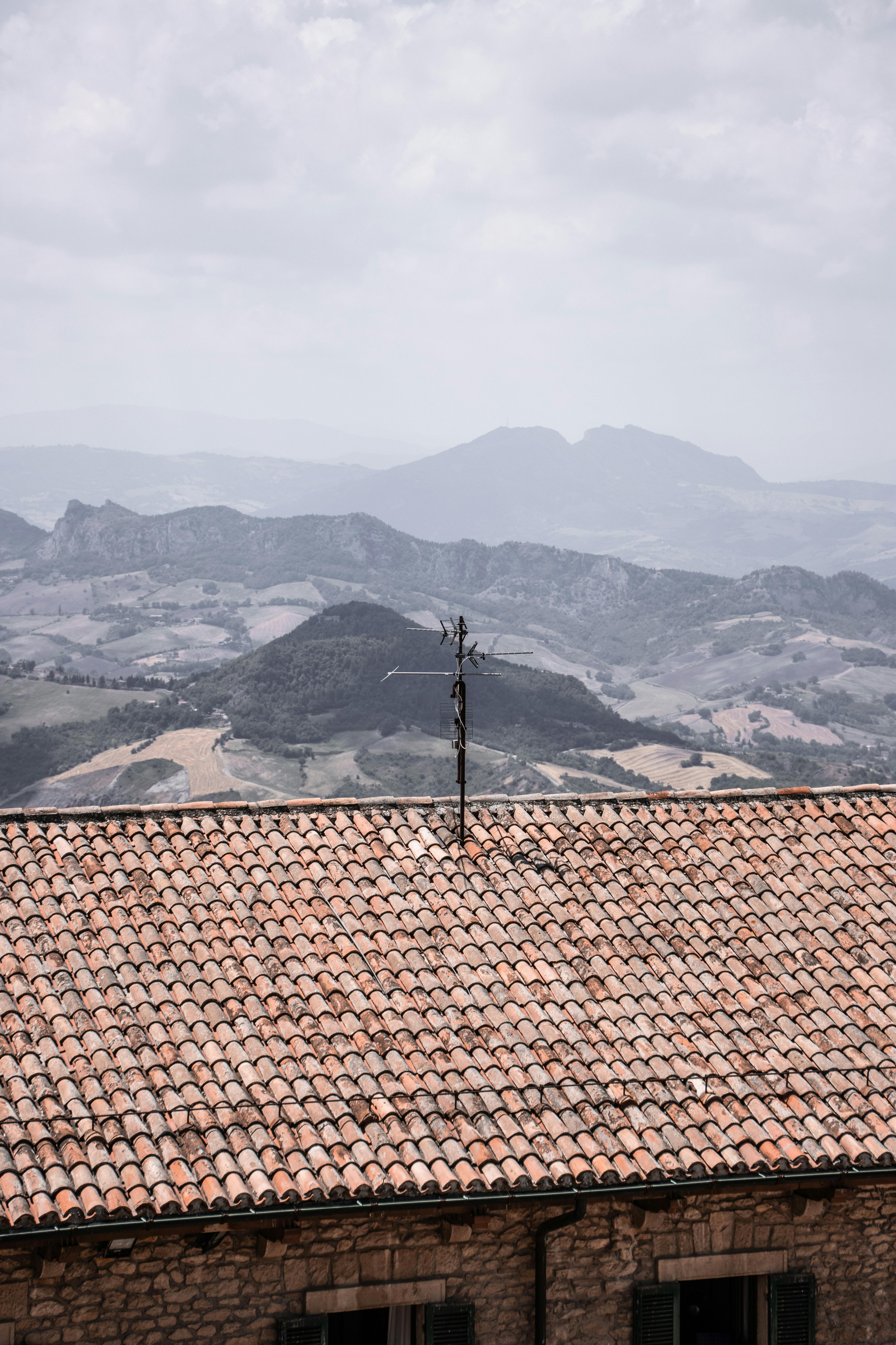 A traditional tiled rooftop with an antenna, overlooking the rolling hills of San Marino.
