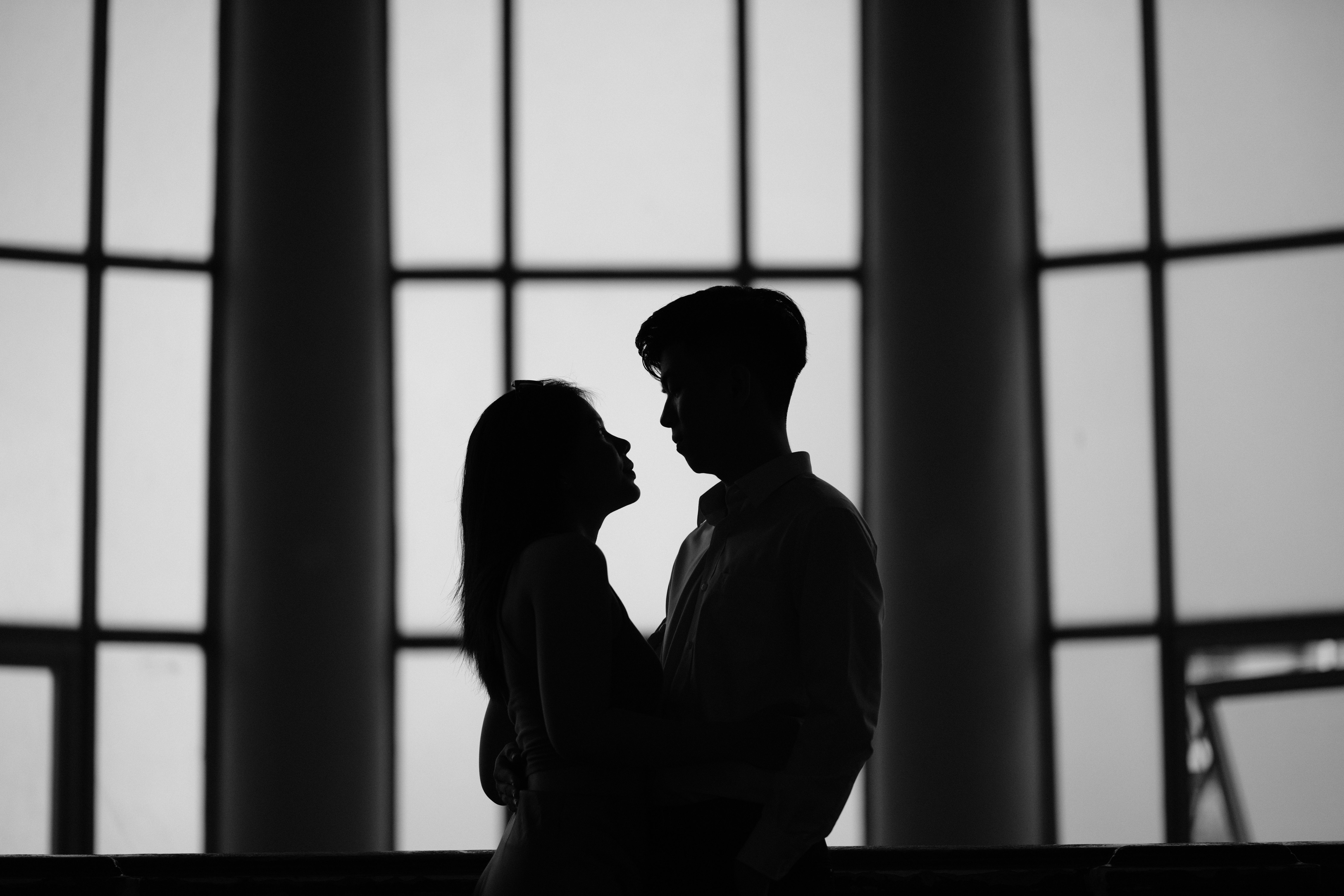 A couple embraces in a striking black and white silhouette, indoors.