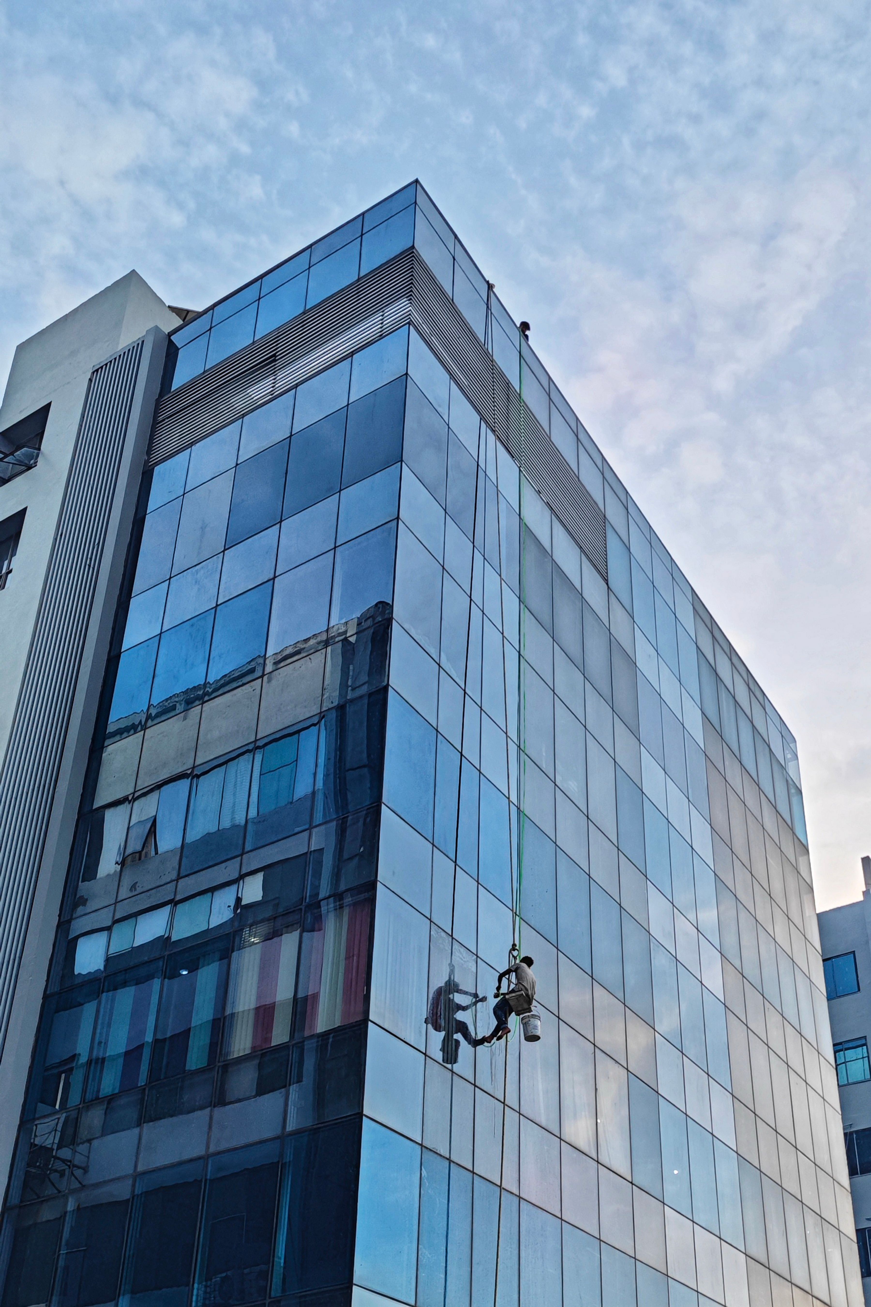 Window cleaners working on a tall glass building in an urban setting during the daytime.