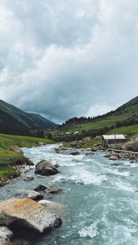 Serene mountain river through lush green valley under a cloudy sky, perfect for travel enthusiasts