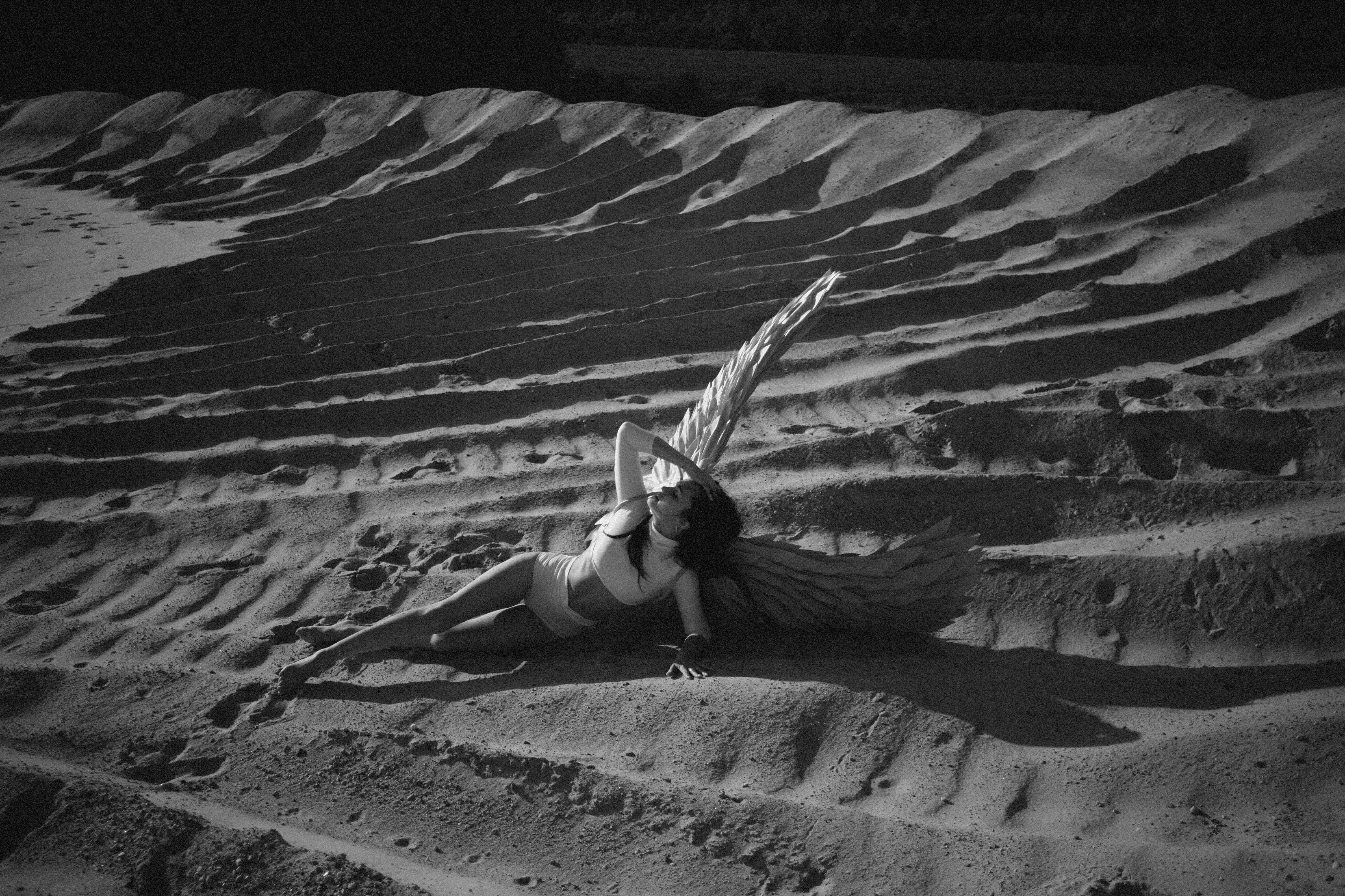 A woman in a white dress sitting on the sand with wings · Free Stock Photo