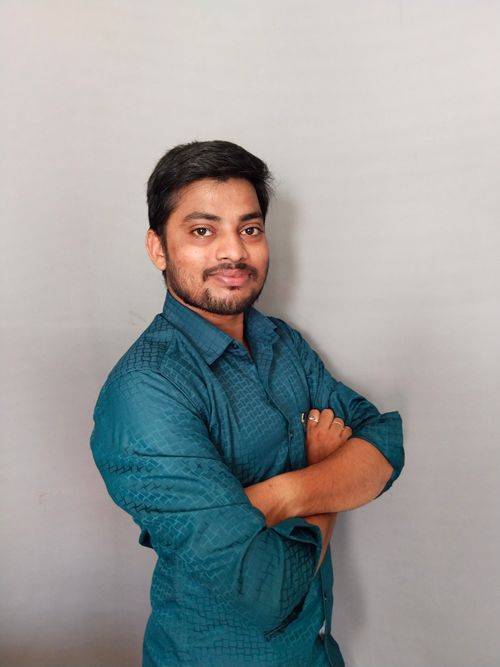 Free A confident young man with a big smile, dressed in a teal shirt, standing against a plain background. Stock Photo