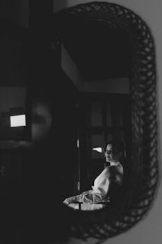 Artistic black and white portrait of a woman reflected in a mirrored interior setting.