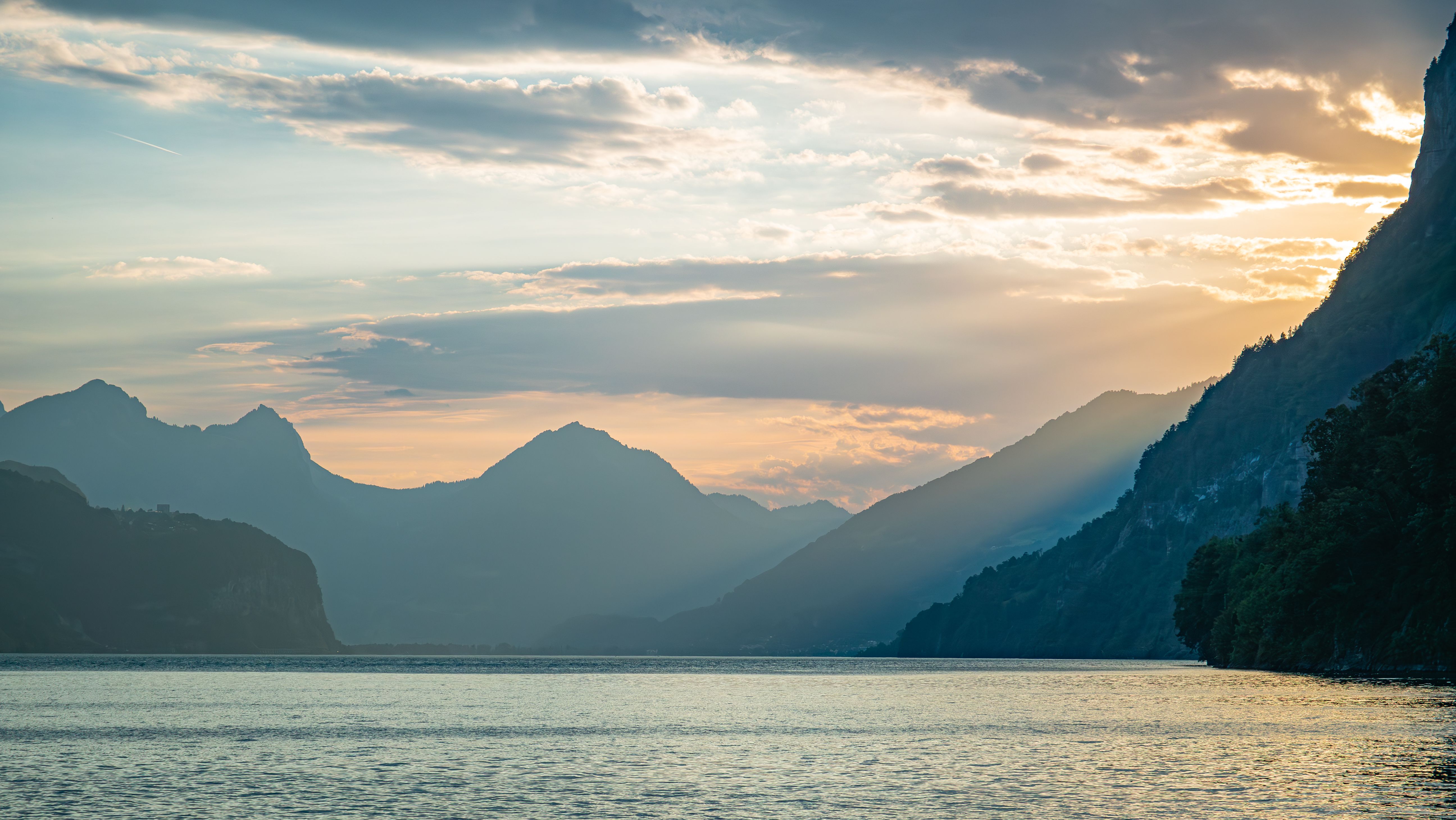 Peaceful sunset over lake with mountain silhouettes and soft light rays in Weesen, Switzerland.