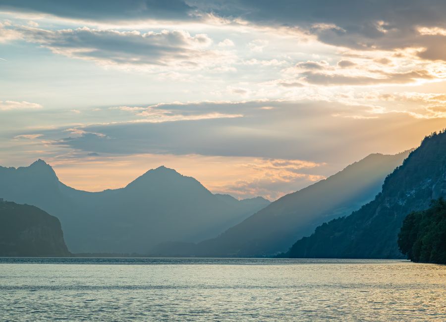 Peaceful sunset over lake with mountain silhouettes and soft light rays in Weesen, Switzerland.