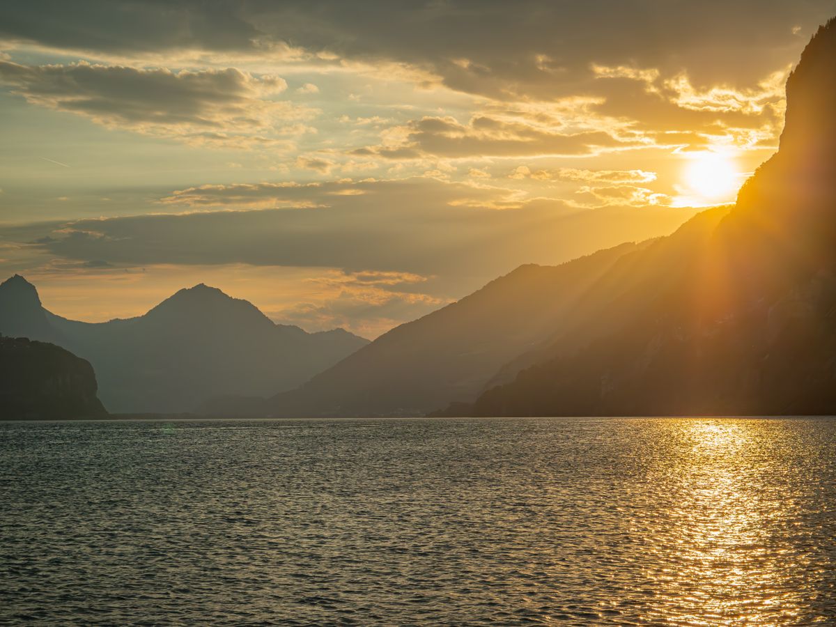 A sunset over a lake with mountains in the background · Free Stock Photo