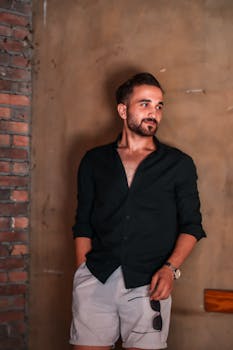 Stylish man in casual attire posing indoors against a brick wall.