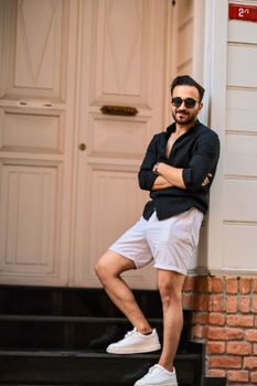 Fashionable man in sunglasses standing casually by a door, showcasing a chic modern look.