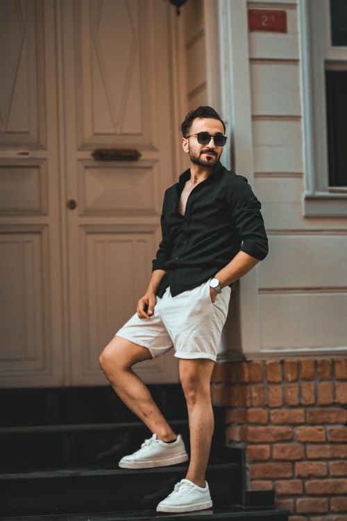 Free Stylish man in black shirt, white shorts, and sunglasses posing outdoors. Stock Photo