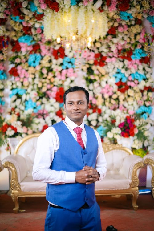 Free Portrait of a man in a blue suit, posing in front of colorful floral wedding backdrop. Stock Photo