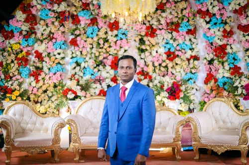 Free Indian wedding with a groom in traditional attire surrounded by vibrant floral decor indoors. Stock Photo