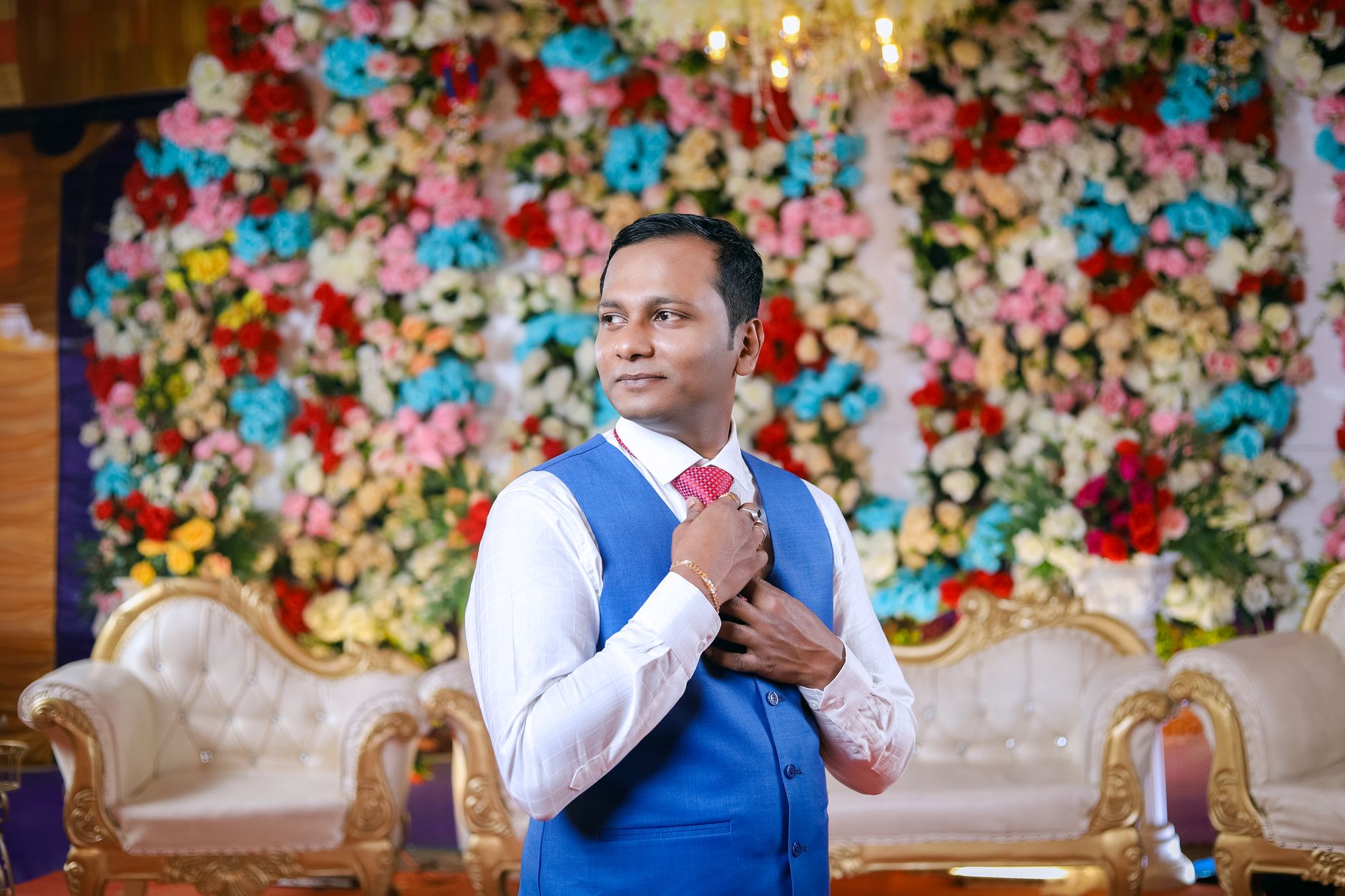 Groom in traditional Indian attire posing elegantly with vibrant floral decorations in the background.